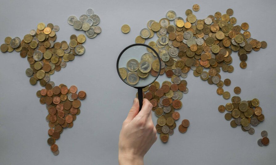 Eine Person hält eine Lupe über eine aus Münzen bestehende Weltkarte