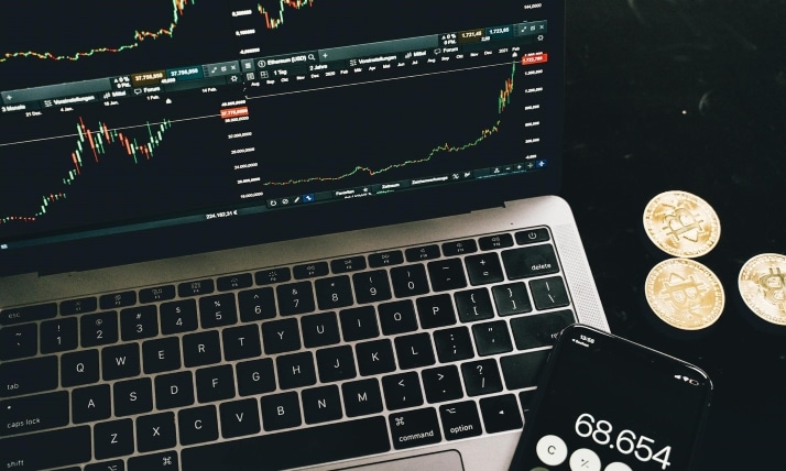 Ein Laptop mit angezeigten Aktienkursen, daneben ein Taschenrechner und Münzen